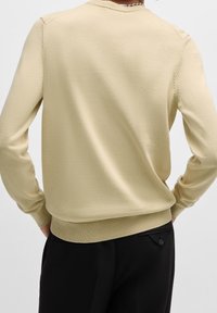 Pull beige clair avec manches longues, encolure ronde, texture lisse et détails côtelés aux poignets et à l'ourlet.