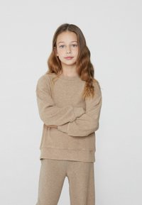 Beżowy sweter z długimi rękawami i okrągłym dekoltem, w połączeniu z dopasowanymi spodniami. Miękka struktura, luźny krój i minimalistyczny design.