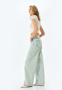 Ljusblå vida jeans med hög midja, med subtil slitning och en klassisk femficksdesign. Matchar med en vit stickad topp.