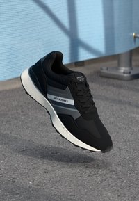 Black athletic sneaker with a textured fabric upper, featuring gray and white accents, a cushioned sole, and a lace-up design.