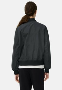 Schwarze Nylon-Bomberjacke mit geripptem Kragen und Bündchen, entspannter Passform und glattem Textil, von hinten gesehen.
