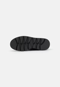 Black rubber shoe sole featuring a textured, multi-directional tread pattern for enhanced grip and flexibility. Smooth finish with logo detail.