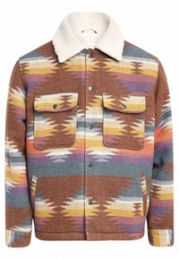Veste marron à motifs multicolores avec un col en sherpa, deux poches poitrine et des boutons pression ; tissu texturé avec des motifs en zigzag.