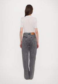 Top blanco de manga corta con texturizado acanalado, combinado con unos jeans de pierna ancha de tiro alto en negro desgastado que cuentan con un parche de cuero en la cinturilla.
