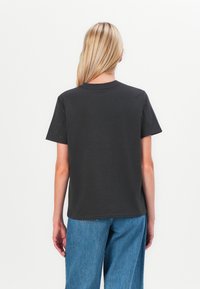 Dark grey t-shirt with short sleeves, round neckline, and subtle texture on shoulders. Paired with loose blue jeans, viewed from behind.