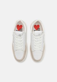 Fehér bőr sneakerek bézs részletekkel, perforált oldalakkal és standard fűzőkkel. Piros és fekete "LOVE MOSCHINO" márkajelzés a talpbetétekben.