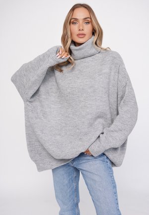 Gray oversized turtleneck sweater with ribbed texture, dropped shoulders, and wide sleeves, paired with light blue jeans.