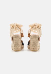 Sandały espadryle z plecionymi beżowymi paskami, czarnymi akcentami z tkaniny i klinem owijanym jutą. Posiadają sznureczki do wiązania wokół kostki.