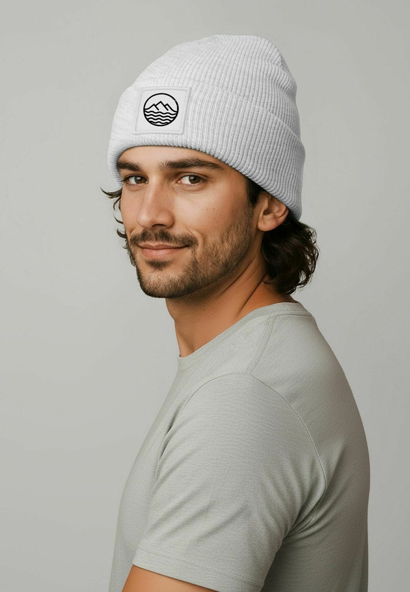 Gray ribbed knit beanie featuring a black patch with a mountain and wave design. Model wears a light gray short-sleeve shirt.