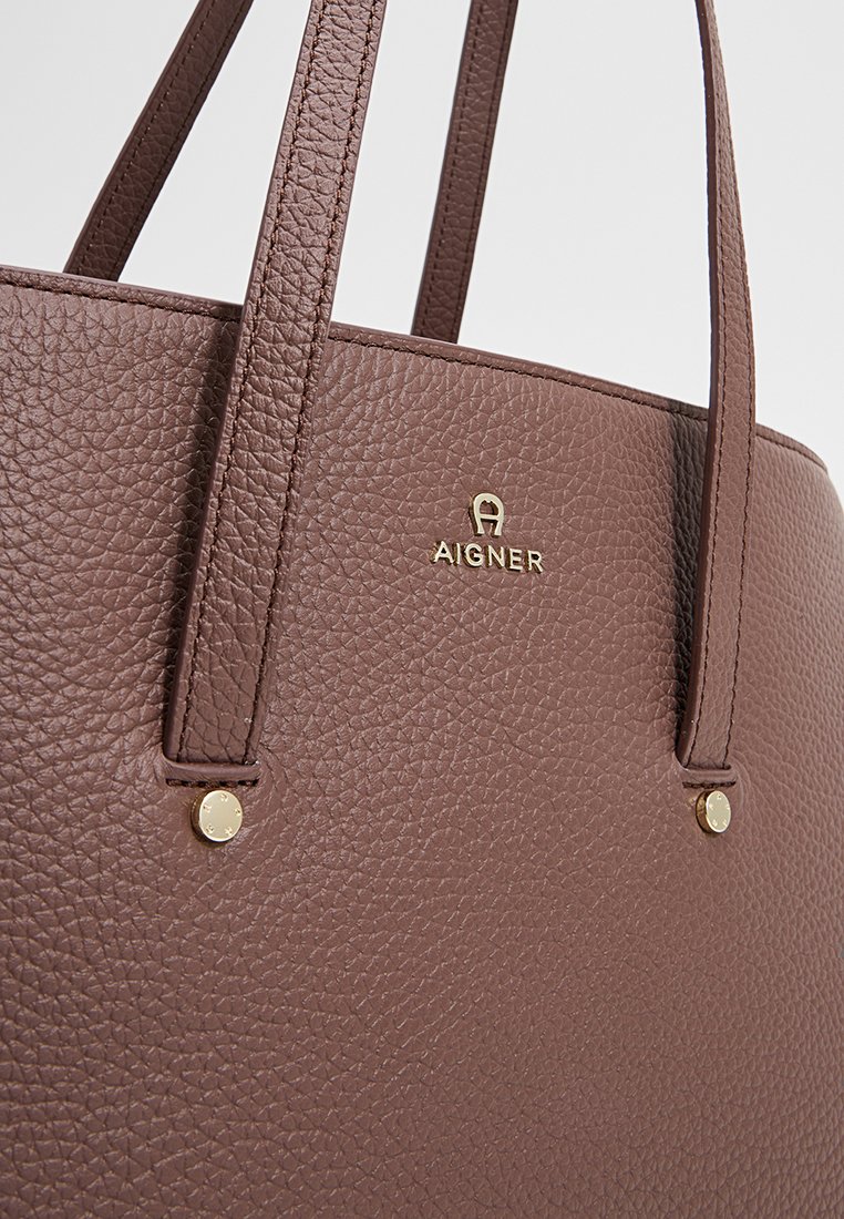 Braune strukturierte Leder-Tote-Tasche mit zwei Griffen, goldenen Hardware-Details und geprägtem Markenlogo auf der Vorderseite.