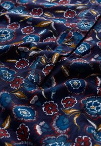 Tejido azul marino con patrón floral que presenta flores azules, rojas y amarillas. Textura suave, detalles de botones y pétalos contorneados.
