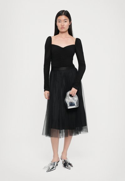 Zwarte lange mouw top met een sweetheart halslijn en gathers, gecombineerd met een tule rok. Houdt een zilver versierde handtas vast en draagt metallic schoenen.