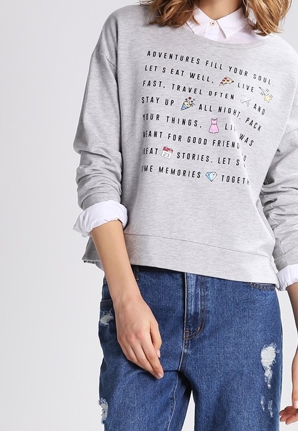 Sudadera gris claro con un diseño corto, que cuenta con una camisa de cuello blanca debajo, y texto impreso con íconos coloridos.