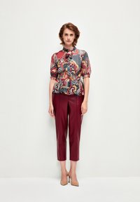 Blusa multicolore con motivo floreale, scollatura rotonda e maniche a sbuffo abbinata a pantaloni cropped in pelle bordeaux e décolleté nude.