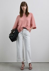 Suéter de punto rosa borroso, pantalones blancos anchos y recortados, bolso de cuero negro y tacones granate con tiras. Tela texturizada y ajuste holgado.