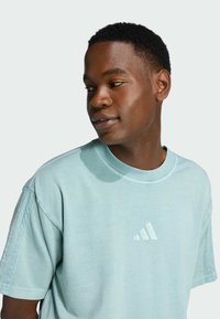 Ανοιχτό μπλε βαμβακερό t-shirt με στρογγυλή λαιμόκοψη και κοντά μανίκια. Διαθέτει κεντημένο λογότυπο τριών ρίγων Adidas στο στήθος.