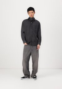 Dark denim button-up shirt with a chest pocket, paired with loose gray jeans. Accessorized with a black bandana and black sneakers.