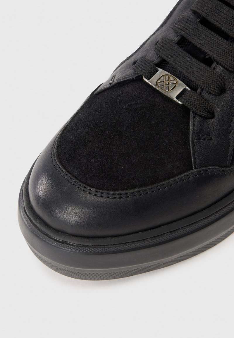 Czarny sneaker z gładkim skórzanym czubkiem i zamszową środkową częścią. Posiada czarne sznurowadła i metaliczny akcent w okolicy języka. Gumowa podeszwa.