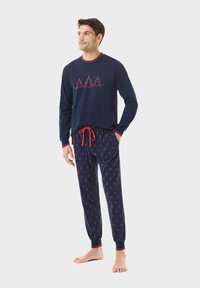 Conjunto de pijama azul marino con parte superior de manga larga, adornada con bordado de árbol rojo y detalles rojos, combinado con pantalones a juego con estampado.