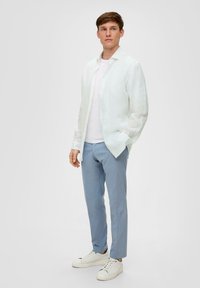 Witte linnen blouse gedragen over een lichtgrijze T-shirt, gecombineerd met lichtblauwe broek en witte sneakers. Eenvoudig, ontspannen fit, zonder patronen.
