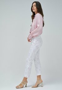 Camisa de manga larga rosa claro con detalles de botones, combinada con pantalones cortos de patrón floral en blanco y sandalias de tacón alto beige con tiras.