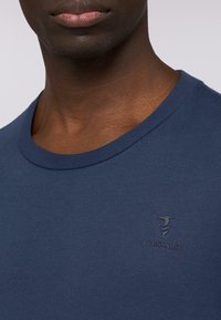 Námořnická modrá bavlněná trička s kulatým výstřihem a krátkými rukávy, s jemně vyraženým logem na hrudi a hladkou texturou.