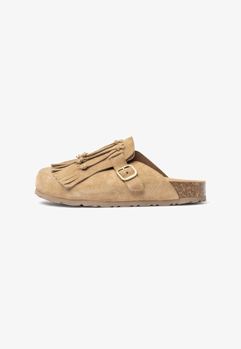 Beige suède muil met een kurken zool, verfraaid met franjes en een gesp detail. Rond neus en open achterdesign voor gemakkelijk aan- en uittrekken.