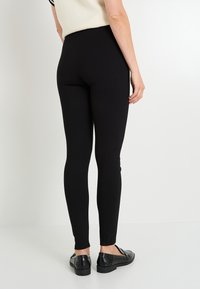Leggings negros hechos de tejido elástico, diseño ajustado, cintura alta y textura suave. Combinados con mocasines negros y brillantes.