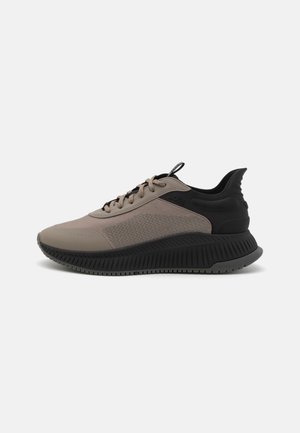 Baskets basses avec dessus en mesh et cuir taupe, col de talon rembourré noir, semelle noire texturée et lacets taupe sur fond blanc.