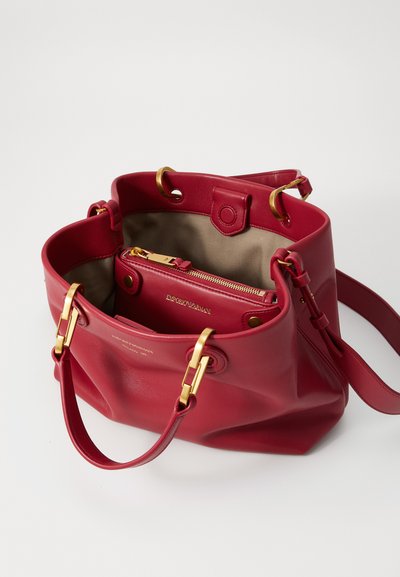 Red leather bucket bag with gold-tone hardware, open top, and interior zip pocket. Smooth texture and minimalist design.