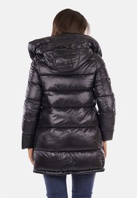 Giacca a vento nera con finitura lucida, texture trapuntata e cappuccio. Caratterizzata da un orlo di lunghezza media e maniche aderenti.