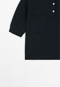 Maglione lavorato a maglia blu navy con maniche corte, dotato di due tasche frontali, un collo alto e due bottoni decorativi. Texture liscia e bordi a coste.