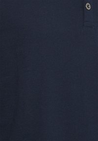 Naviblå piké med en slät textur, som har en treknappsstängning och en subtil lyster. Inga synliga mönster eller accenter.