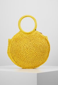 Okrągła, żółta torba ze słomy charakteryzuje się gładkim, teksturowanym wykończeniem, okrągłym kształtem oraz dużą okrągłą rączką do łatwego noszenia.