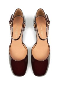 Chaussures en cuir verni bordeaux avec un bout fermé, une bride de cheville et un petit talon carré. Texture lisse et design minimaliste.