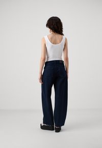 Weißes geripptes Tanktop kombiniert mit dunkelblauen weit geschnittenen Jeans. Die Jeans besitzen eine hohe Taille und zwei Gesäßtaschen, mit fransigen Kanten am Saum.