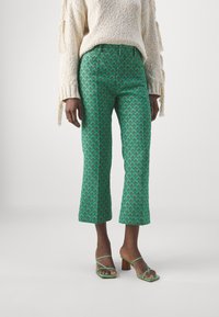 Gröna mönstrade cropped byxor med diamantdesign. Kombinerat med en beige texturerad tröja och gröna sandaler med remmar.