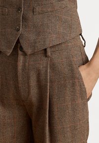 Braun gemustertes Herringbone-Gewebe mit orangefarbenen Streifen; taillierte Weste mit drei Knöpfen; maßgeschneiderte Hose mit Seitentaschen und glatter Textur.