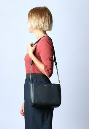Borsa a tracolla in pelle nera con una forma strutturata, cinturino a catena argentata e dettagli in cucitura rossa. Texture liscia e particolare del marchio sulla parte anteriore.