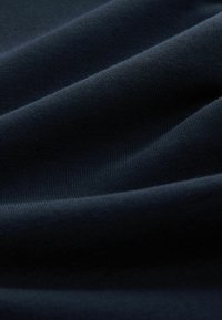 Dunkelmarineblauer Stoff mit glatter Textur, der subtile Falten und rippige Details zeigt. Das Material wirkt weich und biegsam.