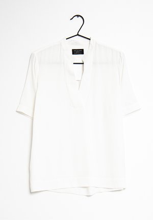 Hvid kortærmet bluse med V-hals og krave, hængende på en sort bøjle mod en hvid baggrund.