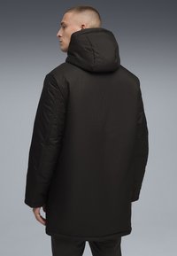 Sort polstret frakke med høj krave og hætte. Har en glat tekstur, lange ærmer og en lige pasform. Minimalistisk design.