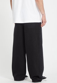 Sorte denim bukser med bred benåpning og falmet tekstur, med to baklommer og subtile stikninger, parret med svarte sneakers.