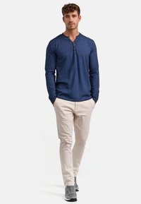 Marineblaues Langarm-Henley-Shirt mit einem geknöpften Ausschnitt, kombiniert mit hellbeigen Hosen und grauen Sneakers. Der Stoff wirkt strukturiert.