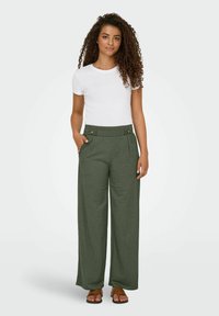 Pantalones verdes de pierna ancha con una cintura alta y detalles de botones, combinados con una camisa blanca de manga corta y sandalias marrones.