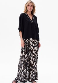 Zwarte losvallende top met een V-hals en contrasterende rand, gecombineerd met wijde broekspijpen met een abstract zwart, wit en bruin patroon.