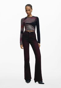 Czarna i czerwona bluzka z długim rękawem w wzory o skróconym kroju, zestawiona z ciemnoczerwonymi spodniami typu dzwony z wysokim stanem oraz czarnymi szpilkami.