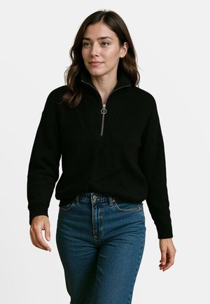 Zwarte gebreide pullover met een kwart ritssluiting en ribbelstructuur; lange mouwen en een relaxed fit, gecombineerd met high-waisted blauwe jeans.