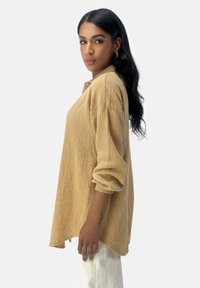 Beige Langarmhemd aus strukturiertem Stoff mit Kragen und Knopfdetails. Oversized-Schnitt mit abgerundetem Saum.
