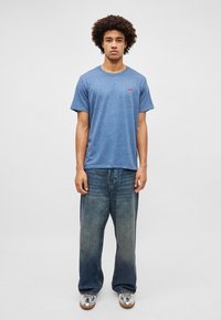 Sinine kanepist kootud T-särk ümmarguse kaeluse ja lühikeste varrukatega, kombineeritud helesiniste laia jalgadega denimitest teksadega ja hõbedaste tossudega.